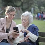 cheerful senior mother and adult daughter using smartphone together