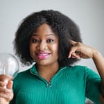 positive young african american lady holding light bulb in hand on gray background