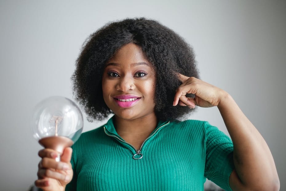 positive young african american lady holding light bulb in hand on gray background