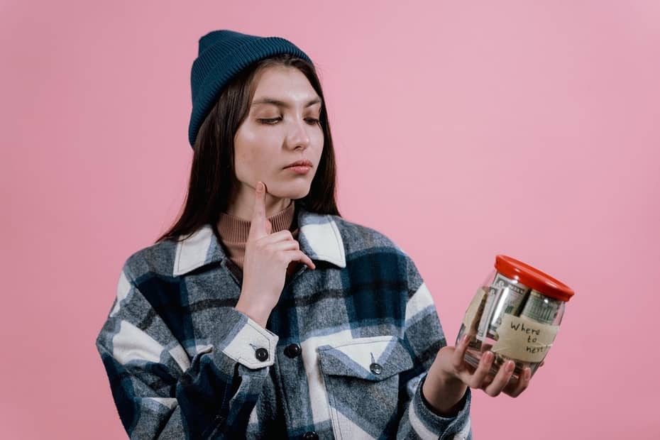 woman in blue plaid long sleeves and knit cap holding a glass jar with money