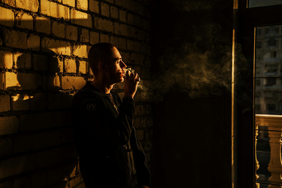 man smoking and leaning on brick wall